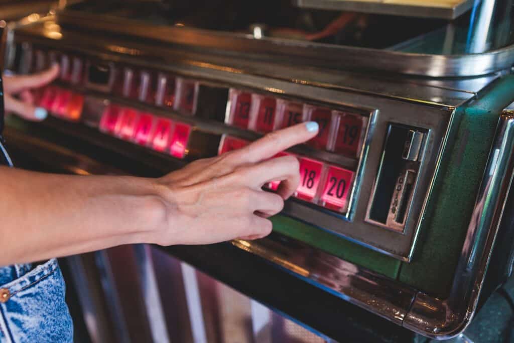 Hand choosing a song on a vintage jukebox with illuminated buttons, paying to play licensed music