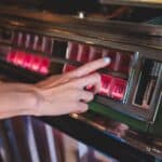 Hand choosing a song on a vintage jukebox with illuminated buttons, paying to play licensed music