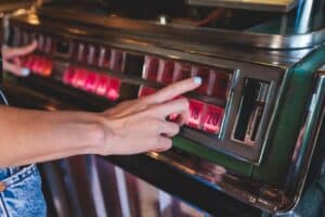 Hand choosing a song on a vintage jukebox with illuminated buttons, paying to play licensed music