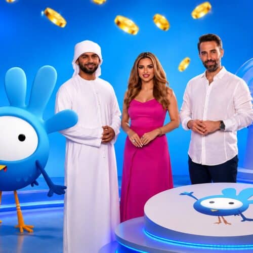 Three Mahzooz presenters on a blue studio set with the bird mascot, gold coins and the draw machine