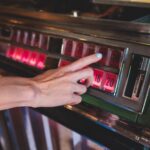 Hand choosing a song on a vintage jukebox with illuminated buttons, paying to play licensed music